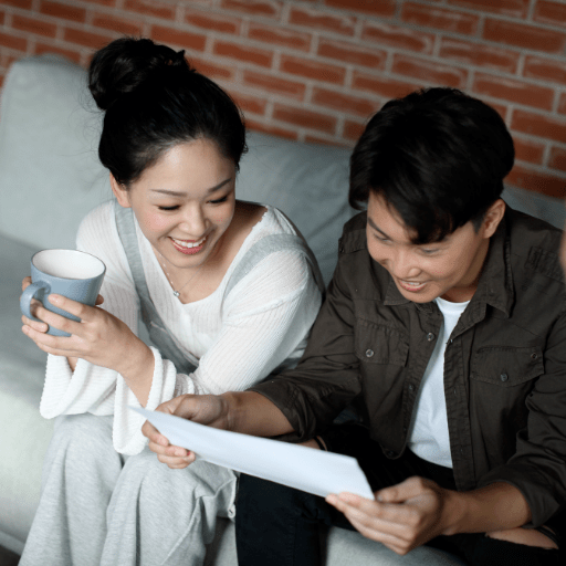 Smiling Asian couple sit on couch and overlook financial papers. About Insurance Planning Concept.