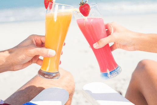 Couple toasting together at the beach on a sunny day. Visualizes the third element of the Netvesco tagline: Achieve