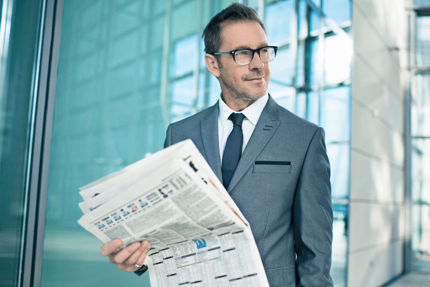 Middle-aged white businessman wearing a gray suit and eyeglasses holding a business newspaper. Financial Planning/ Investment Planning Concept.