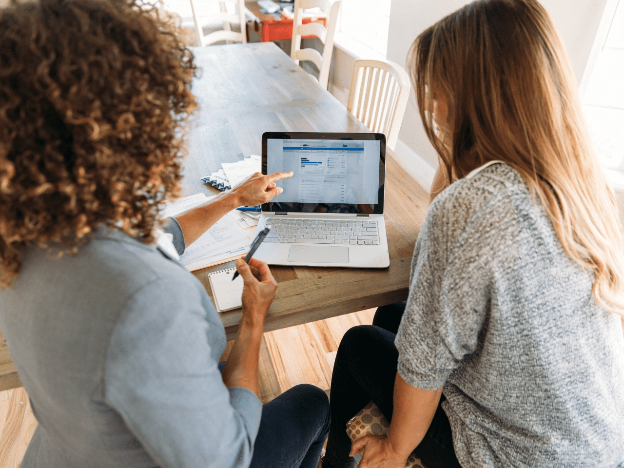 Personal Financial Help with Financial Advisor: A female financial advisor sits with a woman at her dining room table with laptop and financial reports helping her monthly budget and investments. She is showing her client how to read a financial report. Investor Education Concept.