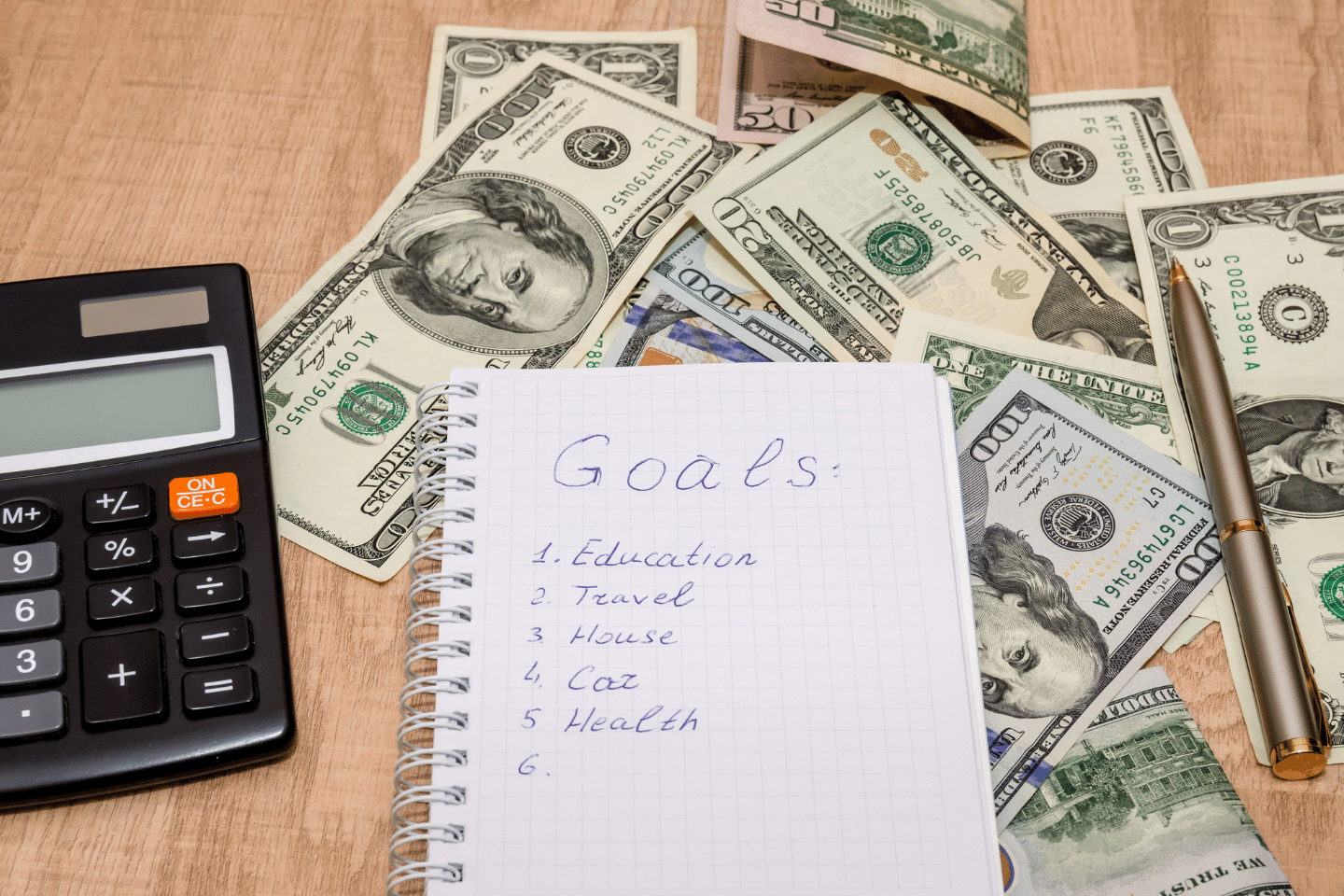 Financial goal concept, word on notepad with dollar bills, calculator, and pen