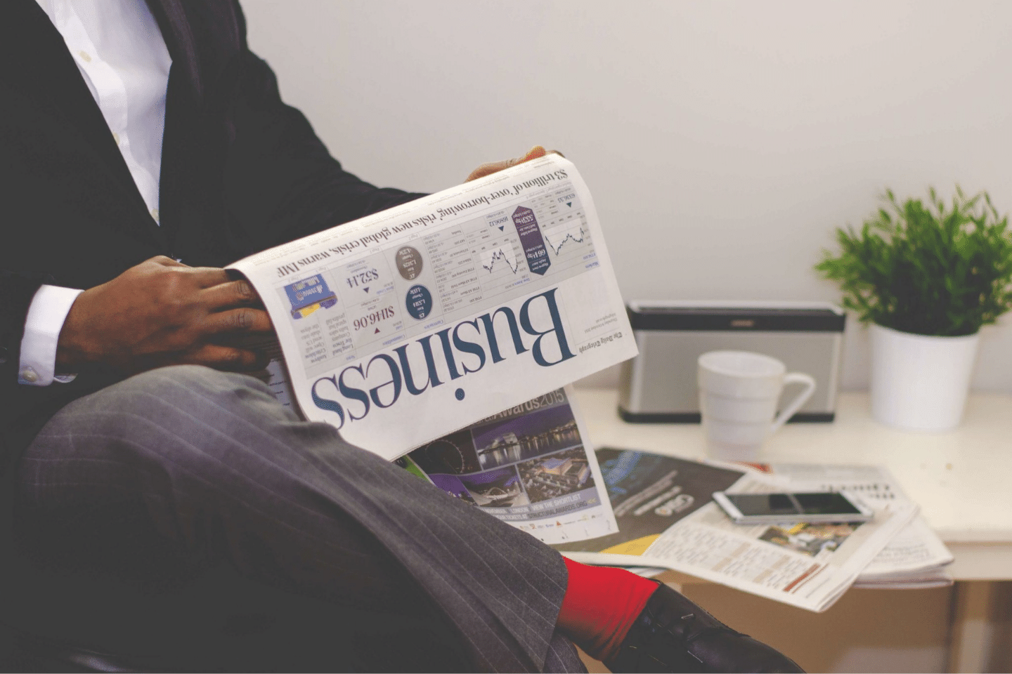 Man Reading Newspaper While Sitting Near Table With Smartphone and Cup.