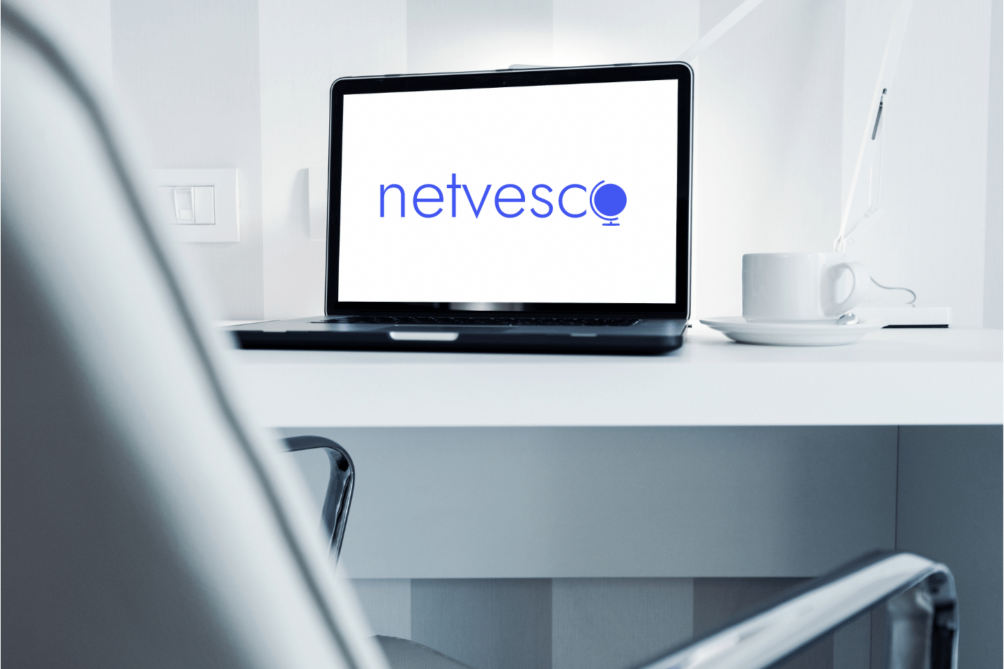 Modern Office Workstation With Laptop Computer. Clean white desk and chair. Welcome to Netvesco. Editorial Policy Concept.